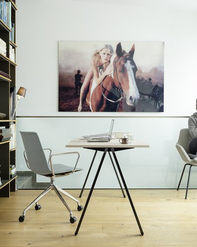 Desk with swivel chair. Woman is sitting behind it at the window and on the phone.