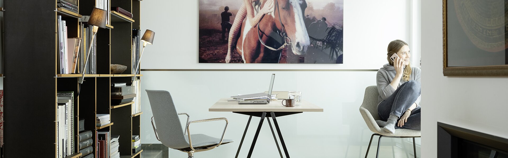 Desk with swivel chair. Woman is sitting behind it at the window and on the phone.