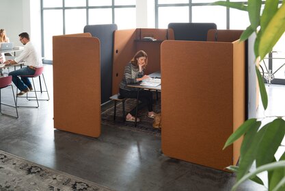 Frau arbeitet in einer Meeting Box, eingegrenzt durch Paravents.